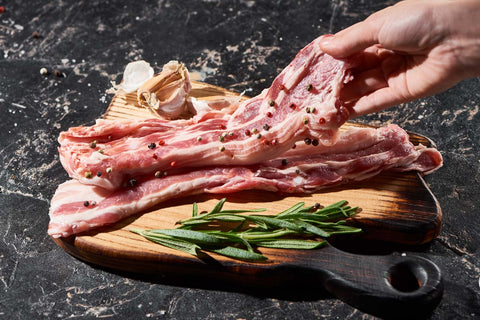 Fresh Iberico pork slices on a wooden board with rosemary, garlic, and peppercorns, highlighting Spanish culinary tradition.