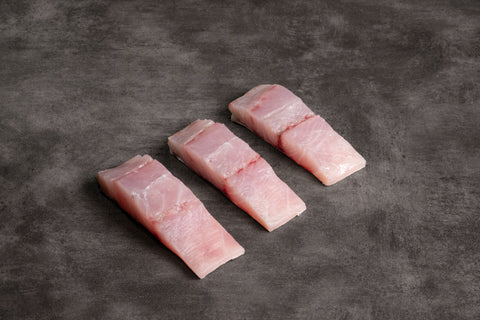 Three raw fish fillets on a dark gray surface