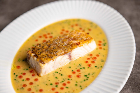 Plated dish of fish fillet with a yellow sauce on a white plate.