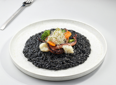 Black rice dish with vegetables on a white plate