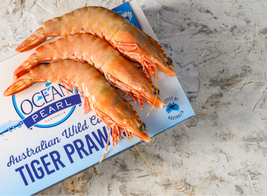 Three tiger prawns on a package labeled 'Ocean Pearl Australian Wild Catch Tiger Prawns' on a marble surface.