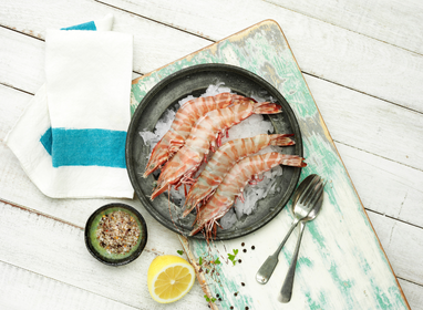 Raw shrimp on a plate with lemon, salt, and pepper on a wooden surface