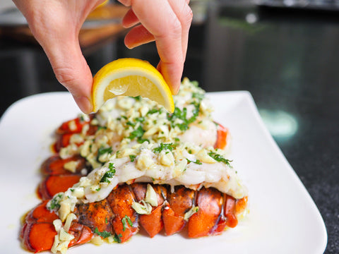 Person adding a lemon wedge to a dish of lobster tail on a white plate.