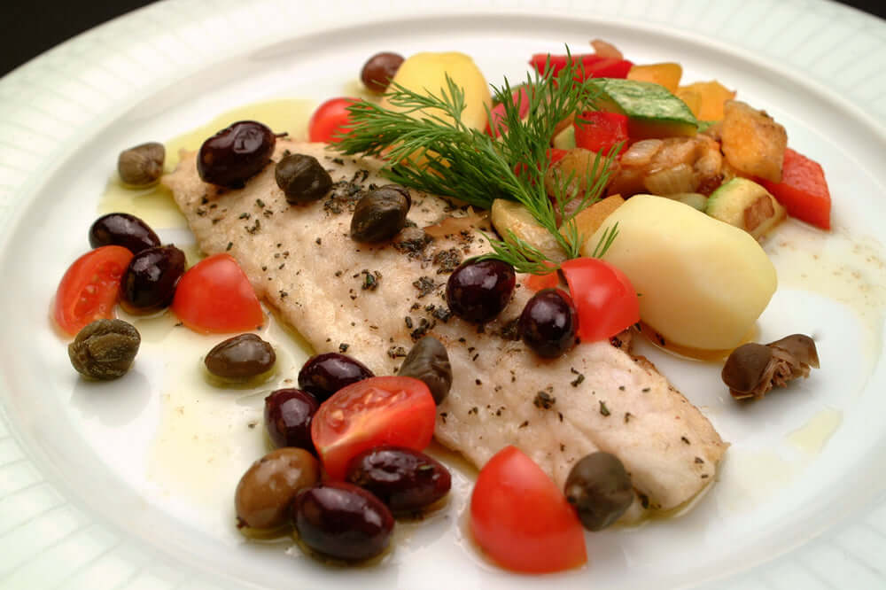 A skin off branzino fillet cooked  and plated with tomatoes and olives
